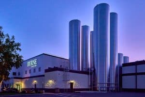 Byrne DeWitt plant at dusk. The plant is a cream and brown building with a lighted BYRNE logo and several gleaming silver silos
