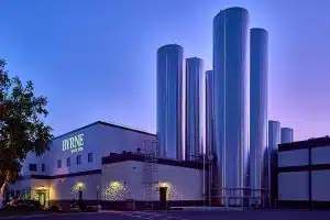 Byrne DeWitt plant at dusk. The plant is a cream and brown building with a lighted BYRNE logo and several gleaming silver silos